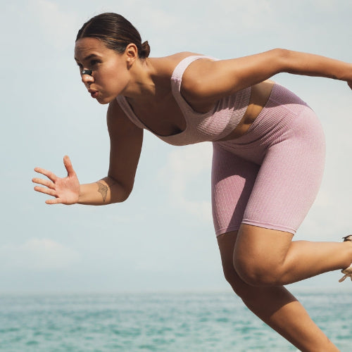 Woman in pink athletic wear running on a beach with clear sky and water in the background